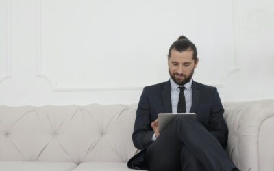 Un homme d'affaires en costume assis sur un canapé utilisant une tablette, souriant.