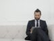 Un homme d'affaires en costume assis sur un canapé utilisant une tablette, souriant.