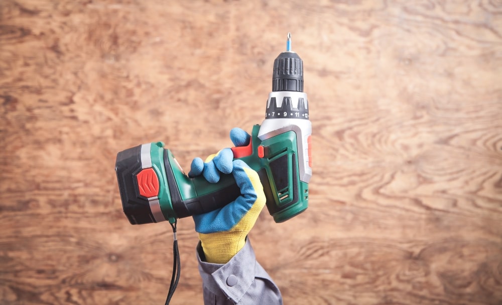 Main gantée tenant une perceuse-visseuse sans fil, représentant l'innovation technologique pour l'efficacité des chantiers